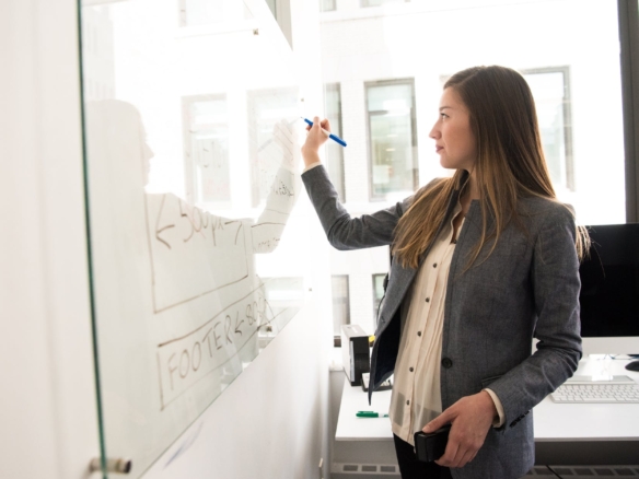 woman wearing gray blazer writing on dry erase board